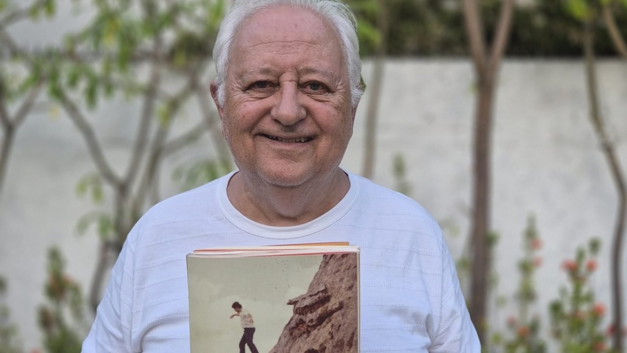 Caio Tibúrcio sorrindo, segurando livro e de blusa branca — Foto: 1 de 1 Imagem