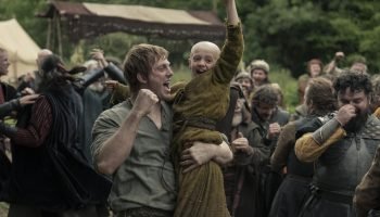 Homem segura criança careca no colo em cena da série O Cavaleiro dos Sete — Foto