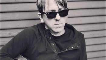 Greg Brown de óculos escuros segurando guitarra — Foto: 1 de 1 Greg Brown de ócu