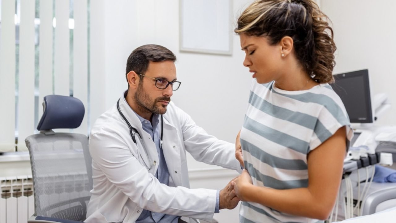Patient telling physician about her pain and health problems during visit to hospital. Young woman complaining about back or kidney ache while sitting on examination bed at the doctor's office